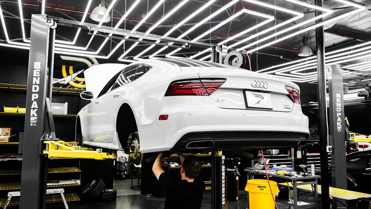 White luxury car being serviced by mechanic in a modern garage setting.